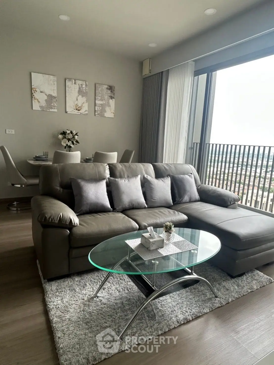 Modern living room with sleek leather sofa and glass coffee table, offering a stunning city view from the balcony.