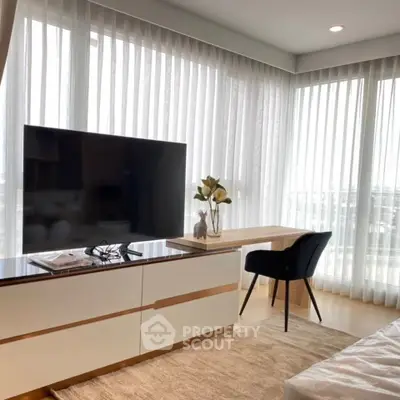 Modern living room with large TV, stylish furniture, and floor-to-ceiling windows offering natural light.