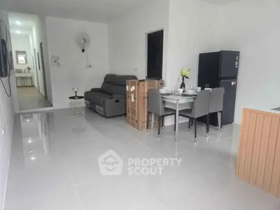 Modern living room with sleek furniture and open layout, featuring a dining area and new appliances.