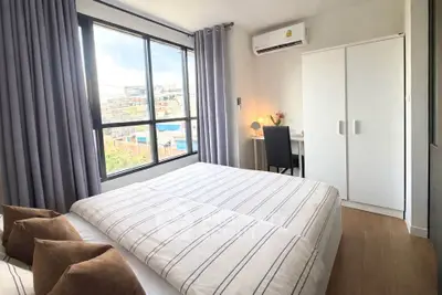 Modern bedroom with large window, stylish decor, and natural light in urban apartment.