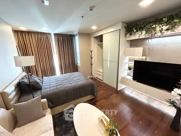 Modern bedroom with cozy decor and large TV, featuring elegant lighting and wooden flooring.