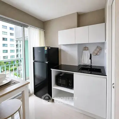 Modern compact kitchen with sleek black appliances and balcony view in urban apartment.