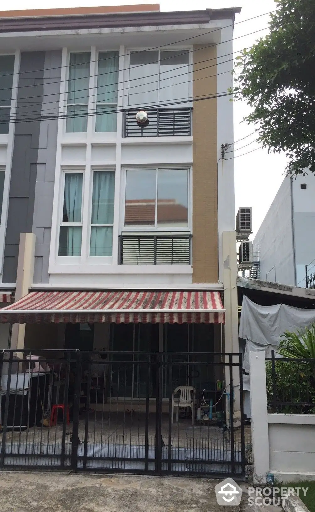 Modern townhouse with striking gray facade and contrasting beige accents, featuring large windows and a secure gated entrance with a covered parking area.