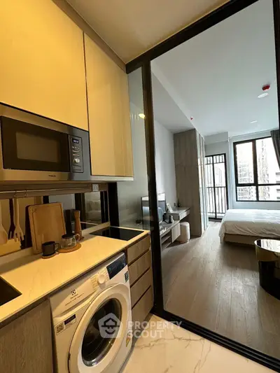 Modern studio apartment with sleek kitchen and cozy bedroom, featuring a washing machine and microwave.