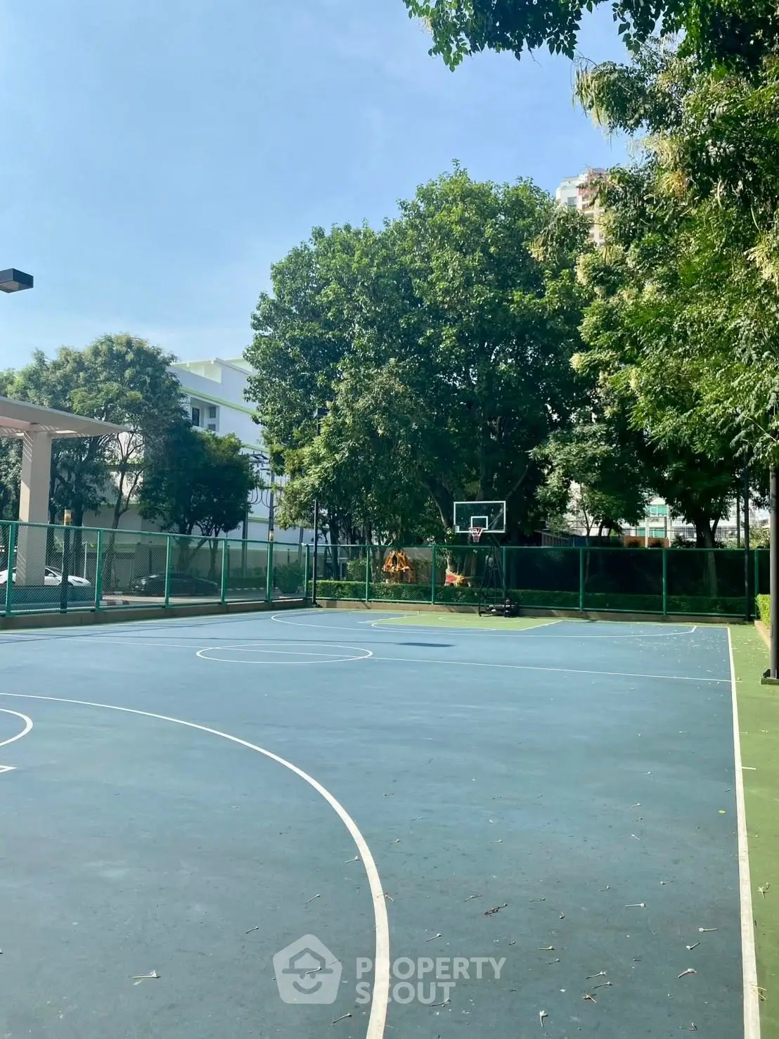 Spacious outdoor basketball court surrounded by lush greenery in a modern residential complex.