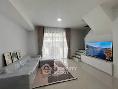 Modern living room with sleek design, large TV, and cozy seating area under staircase.