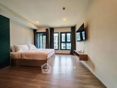 Spacious modern bedroom with large windows and wall-mounted TV in a stylish apartment.