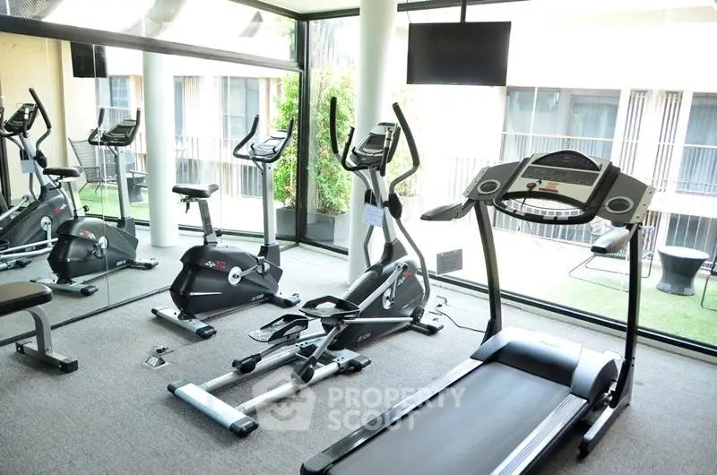 Modern gym with exercise equipment in a bright, glass-walled room.