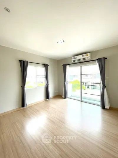 Spacious empty room with wooden flooring and large windows, perfect for customization.