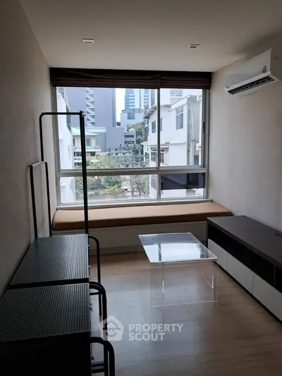 Modern living room with large window and city view, featuring minimalist furniture and air conditioning.