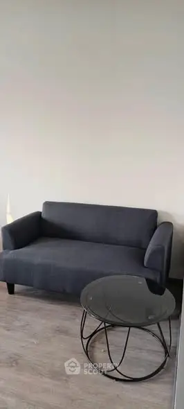 Modern living room with stylish dark sofa and sleek glass coffee table on wooden floor.