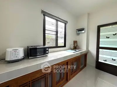 Modern kitchen with sleek countertop, microwave, and rice cooker, featuring a large window for natural light.