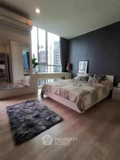 Spacious modern bedroom with large windows and city view, featuring stylish decor and cozy ambiance.