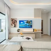 Modern living room with stylish decor and large TV, featuring elegant lighting and cozy seating.