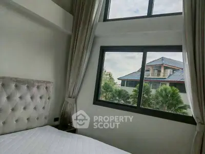 Bright bedroom with large windows offering a scenic view of neighboring houses and lush greenery.
