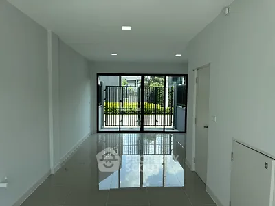 Modern empty room with glossy tiled floor and large sliding glass doors leading to a garden view.