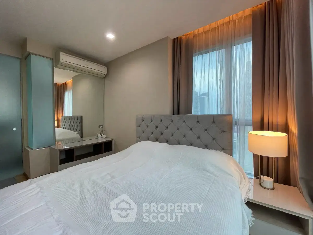 Modern bedroom with elegant decor and natural light, featuring a plush bed and stylish bedside lamp.