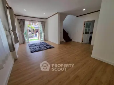 Spacious living room with wooden flooring and large windows opening to a garden view.