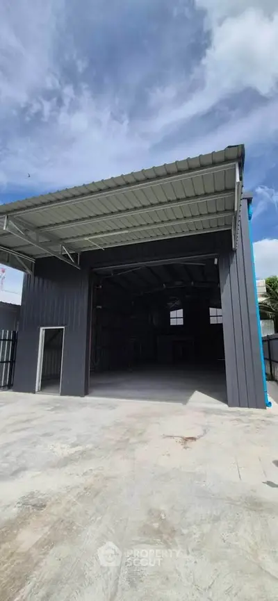 Spacious industrial warehouse with open entrance and modern design under a clear blue sky.