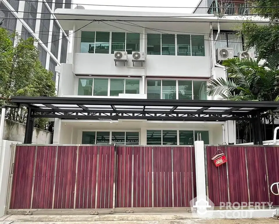 Modern three-story building with gated entrance and lush greenery in urban setting