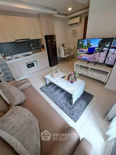 Modern open-plan living room with kitchen, featuring sleek furniture and large TV, ideal for contemporary living.