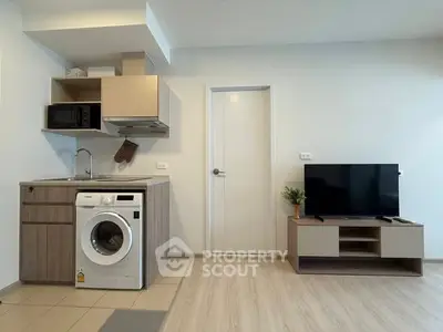 Modern studio apartment with compact kitchen and living area featuring washing machine and TV.