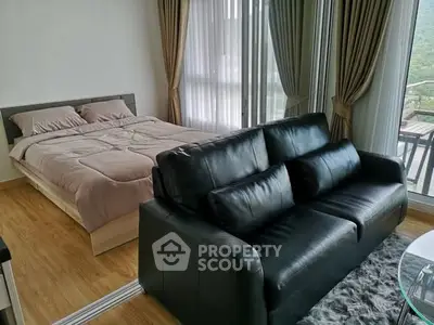 Modern bedroom with stylish black leather sofa and large windows offering scenic views.