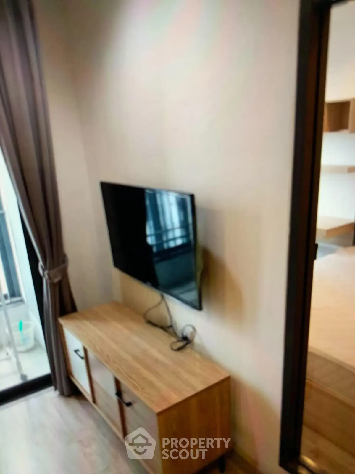 Modern living room with wall-mounted TV and wooden cabinet, featuring a glimpse of a cozy bedroom.