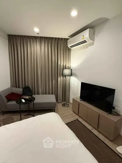 Modern bedroom with cozy seating area and flat-screen TV, featuring elegant curtains and ambient lighting.