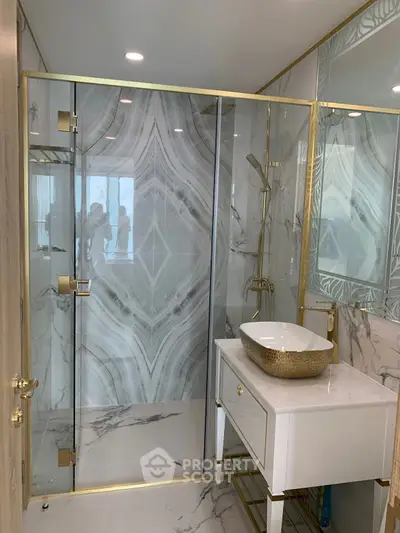 Luxurious bathroom with marble walls and gold accents, featuring a modern glass shower and elegant sink.