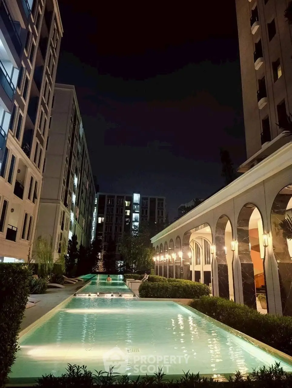 Luxurious apartment complex with illuminated pool and elegant architecture at night.