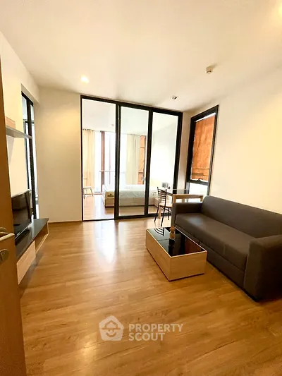 Modern living room with wooden flooring and glass partition leading to bedroom.