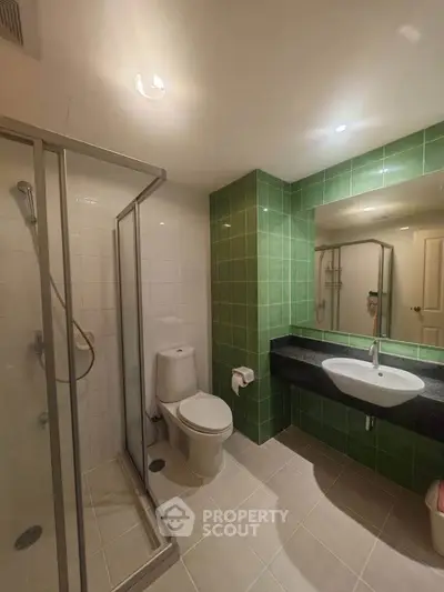 Modern bathroom with green tiles, glass shower, and sleek vanity in a contemporary apartment.