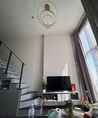 Modern living room with high ceiling and stylish staircase, featuring a large window with natural light.