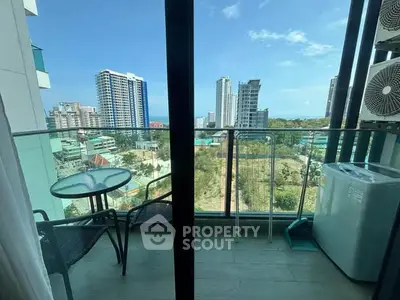 Modern balcony with city view, glass railing, and outdoor seating in high-rise apartment.