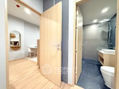 Modern apartment interior with open door to bathroom and study area, featuring sleek design and wooden flooring.