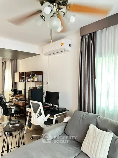 Modern living room with stylish furniture and home office setup, featuring a cozy gray sofa and elegant curtains.