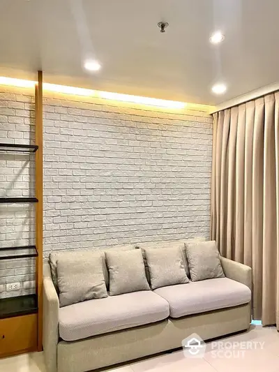 Elegant living room with modern grey sofa against a textured white brick wall, warm ambient lighting, and chic curtains, perfect for urban living.