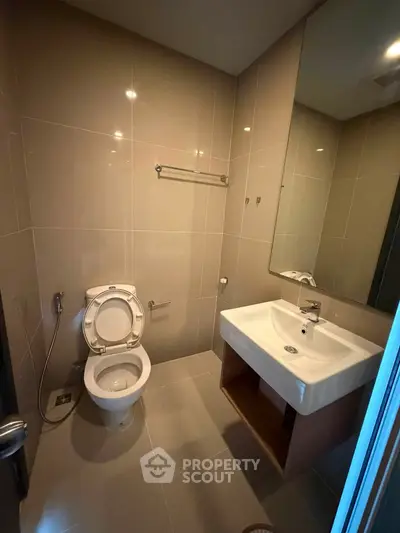 Modern bathroom with sleek fixtures and neutral tiles, featuring a spacious sink and toilet.