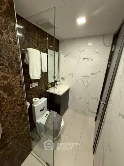 Modern bathroom with marble walls and glass shower enclosure in luxury apartment.