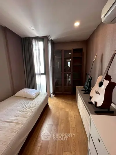 Cozy bedroom with wooden floor, single bed, and guitars, perfect for music lovers.