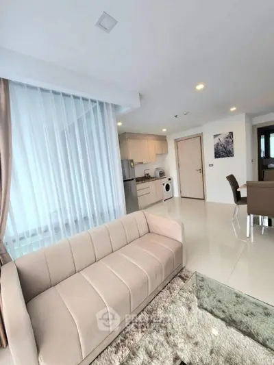 Modern open-plan living room with kitchen and dining area, featuring sleek furniture and natural light.