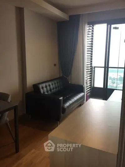 Modern living room with sleek black sofa and balcony view, perfect for urban living.