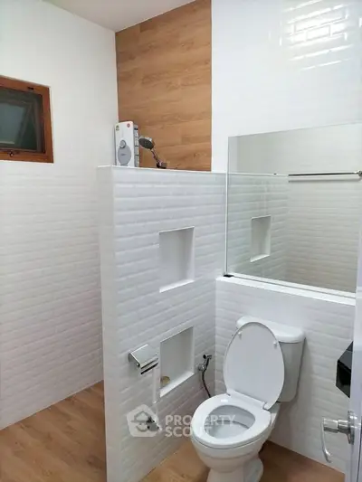 Modern bathroom with white tiles and wood accents featuring a toilet and shower area.