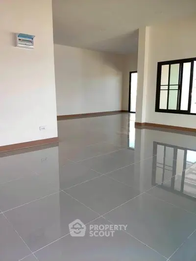 Spacious empty room with glossy tiled flooring and large windows, perfect for customization.
