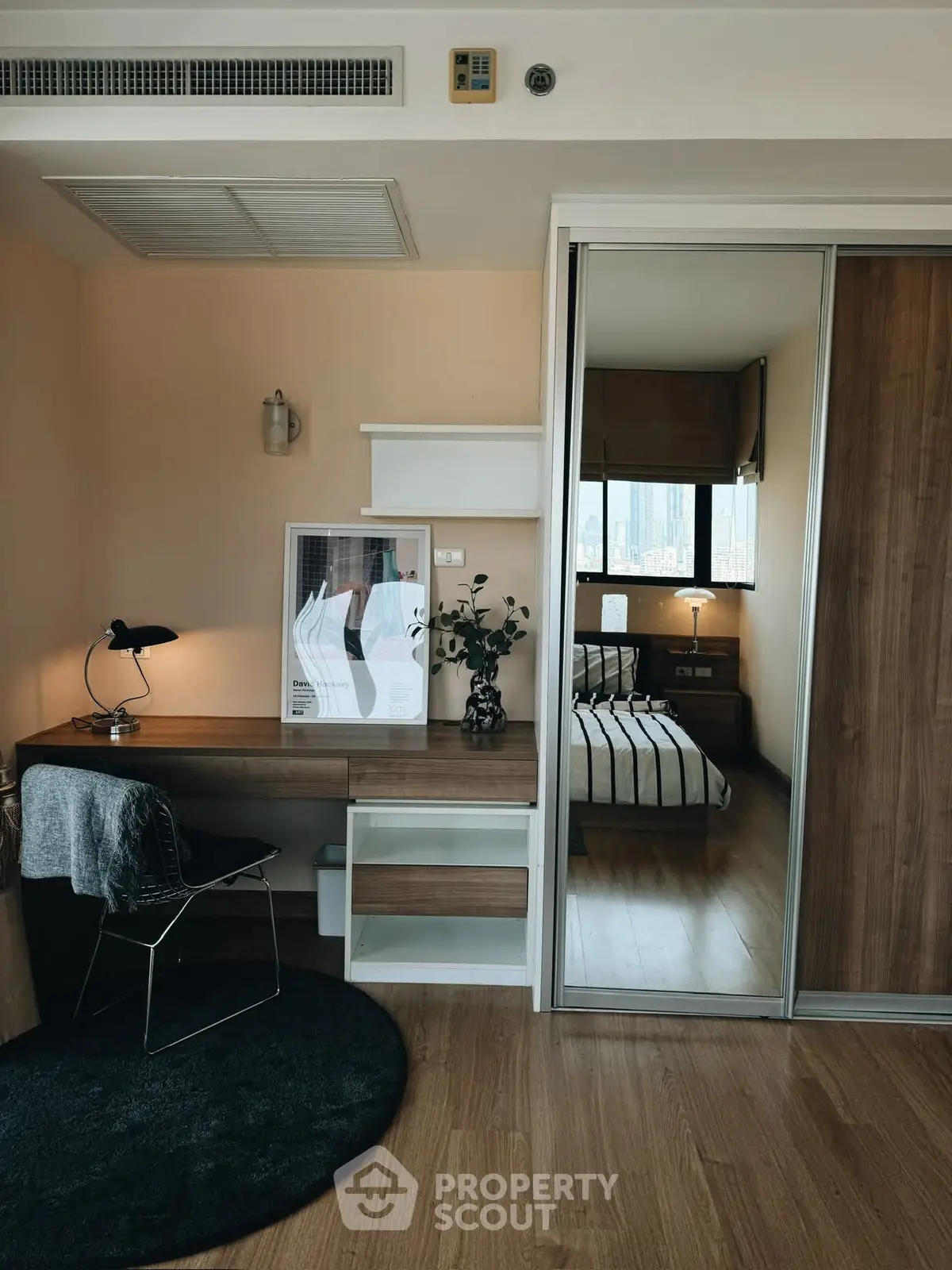 Modern study area with desk and chair adjacent to cozy bedroom with wooden flooring.