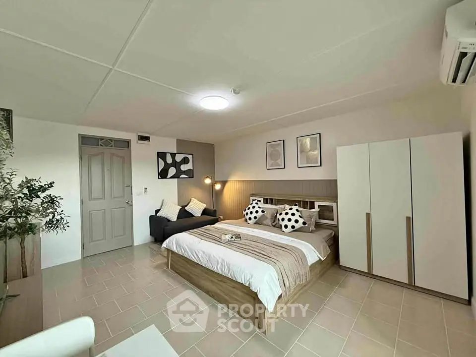 Spacious bedroom with modern decor and ample natural light, featuring a cozy seating area and stylish furnishings.