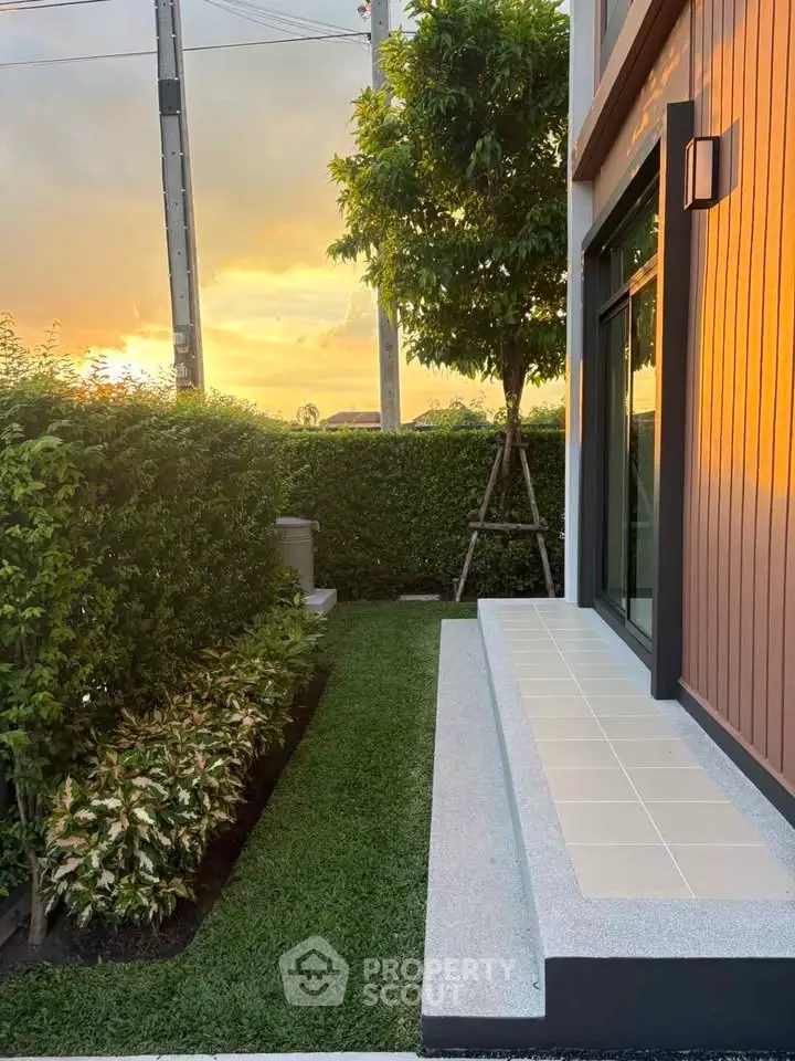 Modern exterior view of a house with lush garden and sunset backdrop, showcasing serene outdoor living.