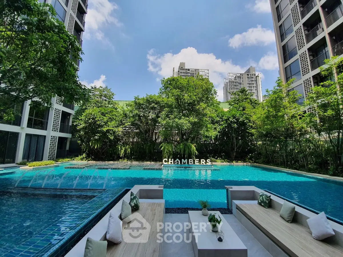 Luxurious poolside view at modern residential complex with lush greenery and clear blue sky.