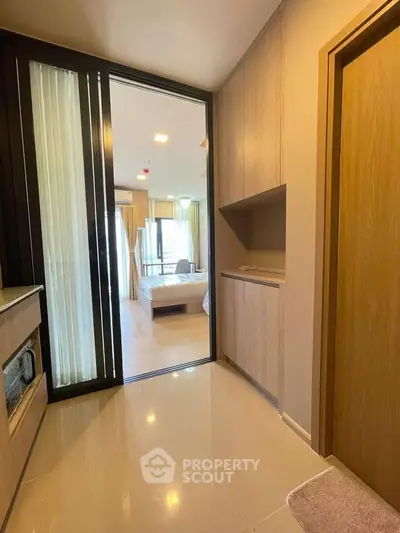 Modern apartment hallway leading to a bright bedroom with large windows and sleek wooden finishes.